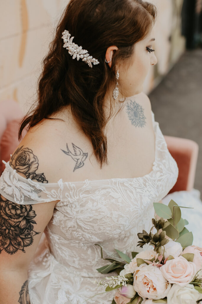 Woman with brown hair and tattoos wearing a off the shoulder wedding gown wedding shoppe berkley mi