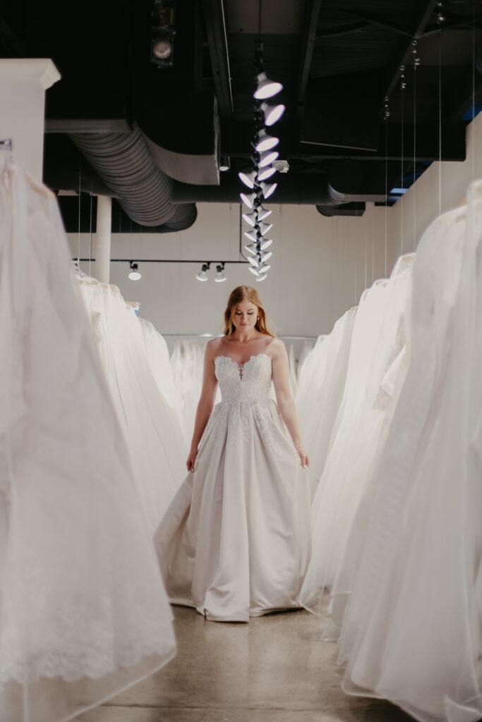 woman walking down aisle of white wedding gowns