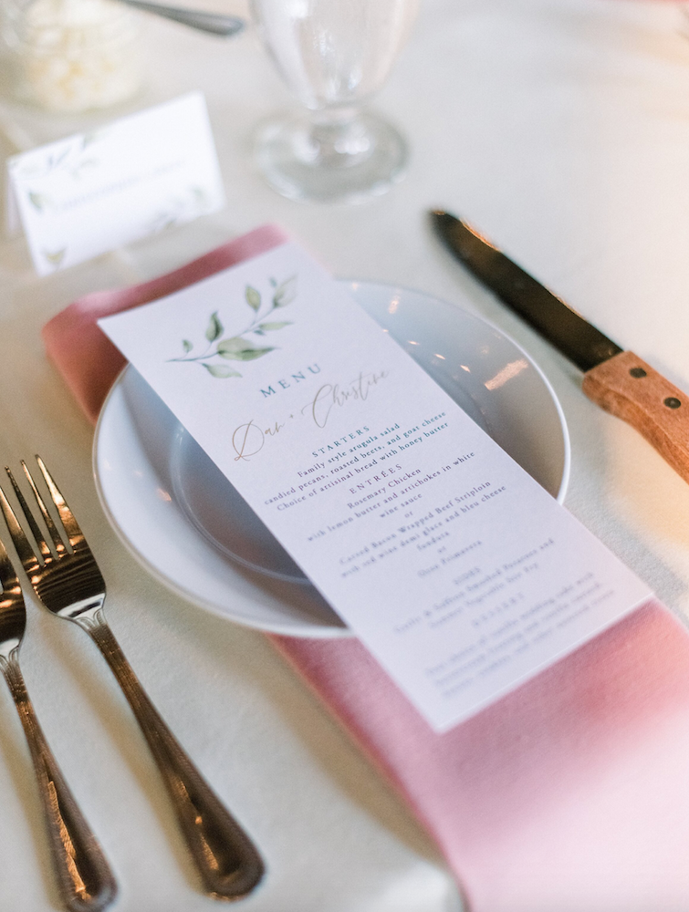 A place setting at a wedding reception with a printed menu on the plate.