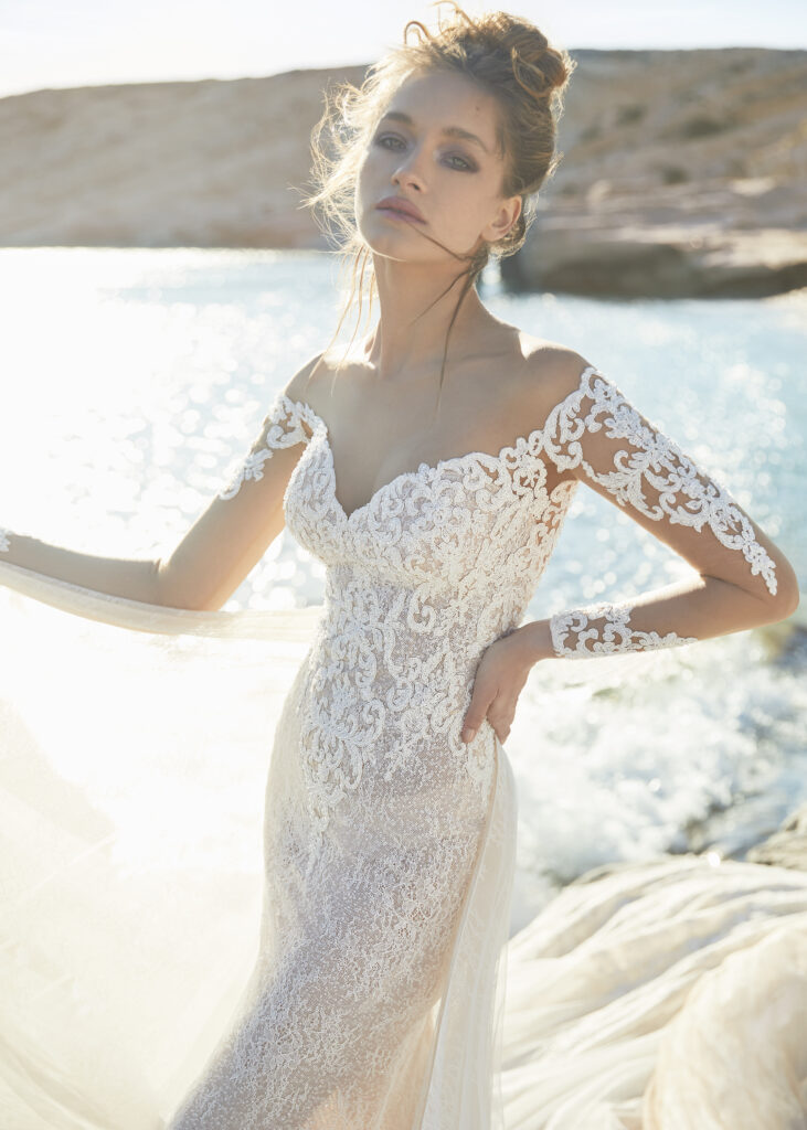 woman posing in fully laced couture wedding dress on cliff overlooking ocean
