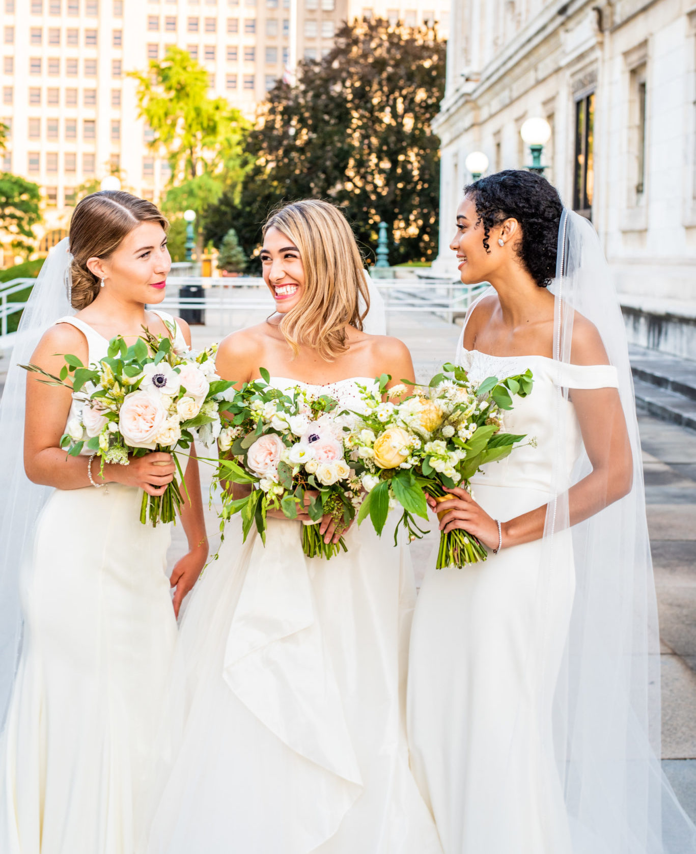 three cheerful women in bridal gowns in metropolitan