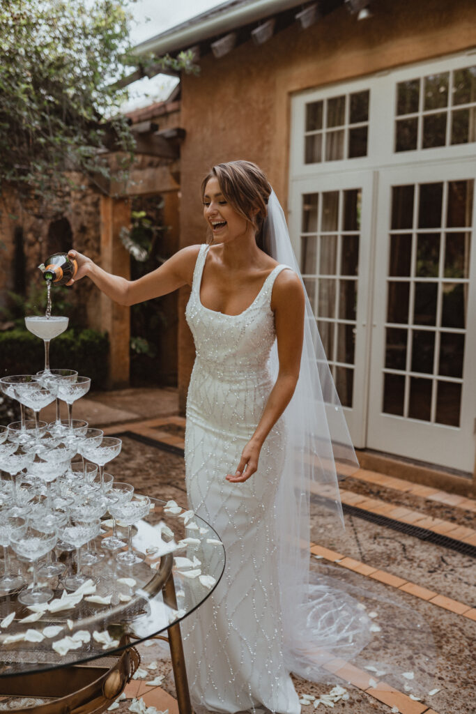 woman in fitted bridal gown pouring champagne in glass