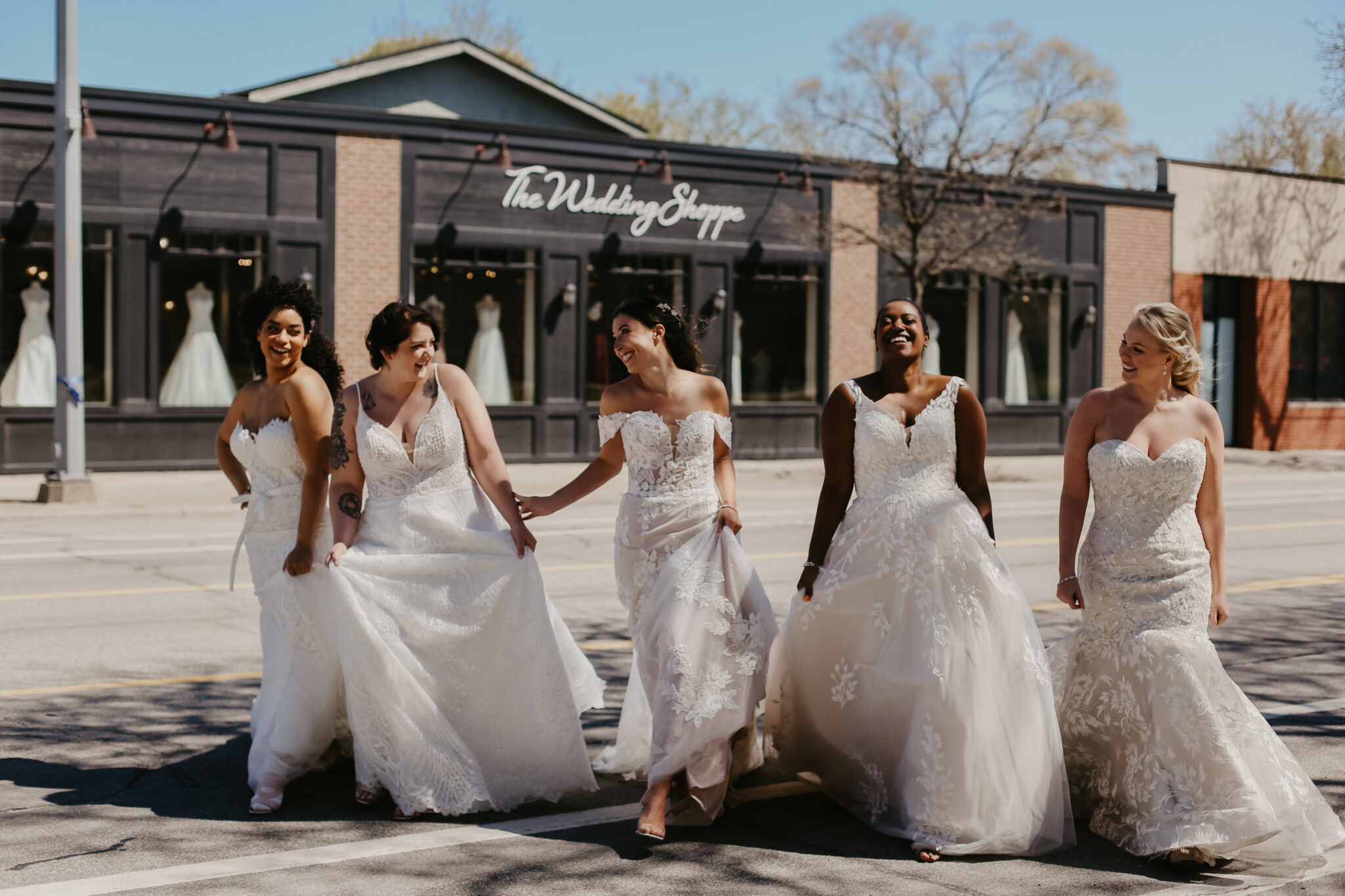 5 woman in bridal gowns in front of The Wedding Shoppe