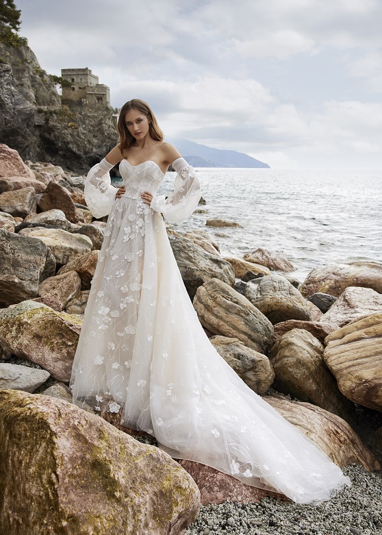 woman standing on rocky coast in lace bridal gown with detached sleeves