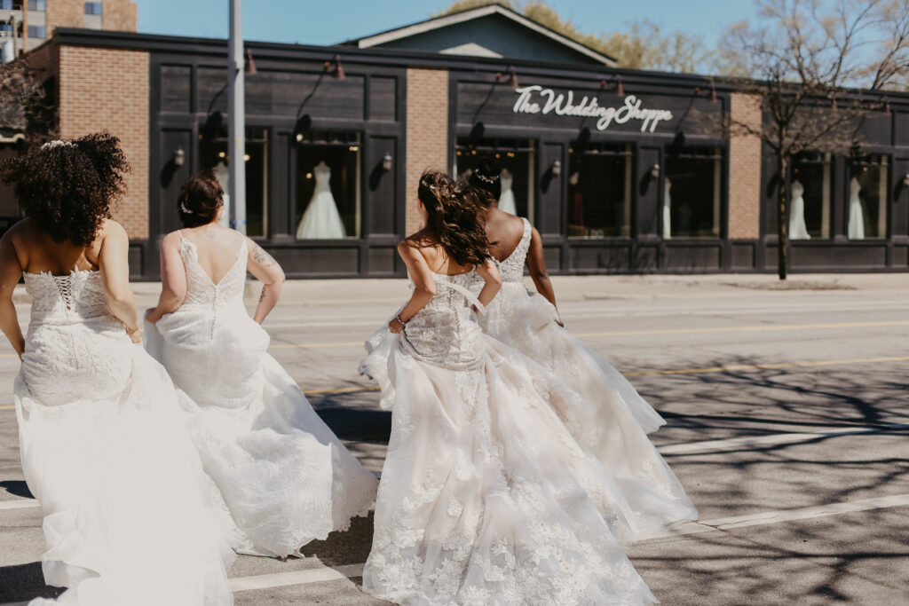 4 brides in bridal gowns running across street to The Wedding Shoppe