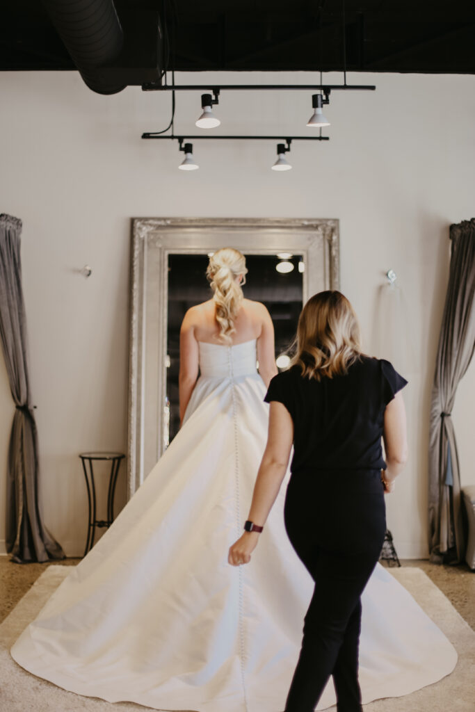bride trying on satin wedding gown with bridal store employee