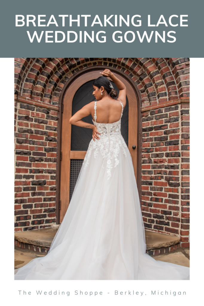 Bride in a long flowing gown with lace straps in a lacey bodice posing in front of a brick building with a wooden door.