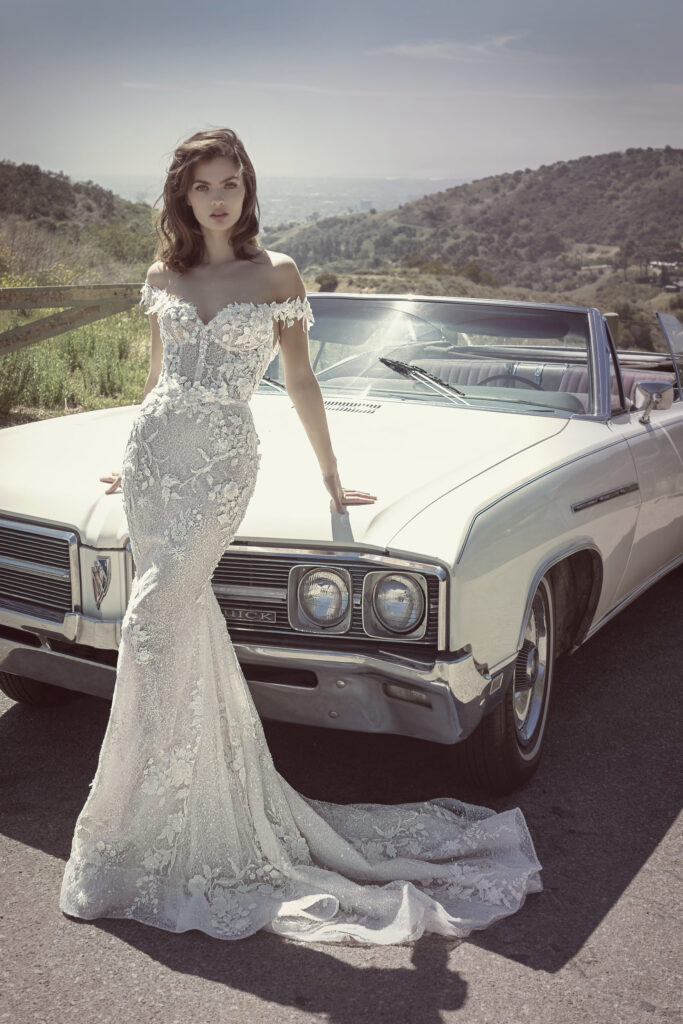 woman in fitted couture designer wedding gown leaning on old fashioned car