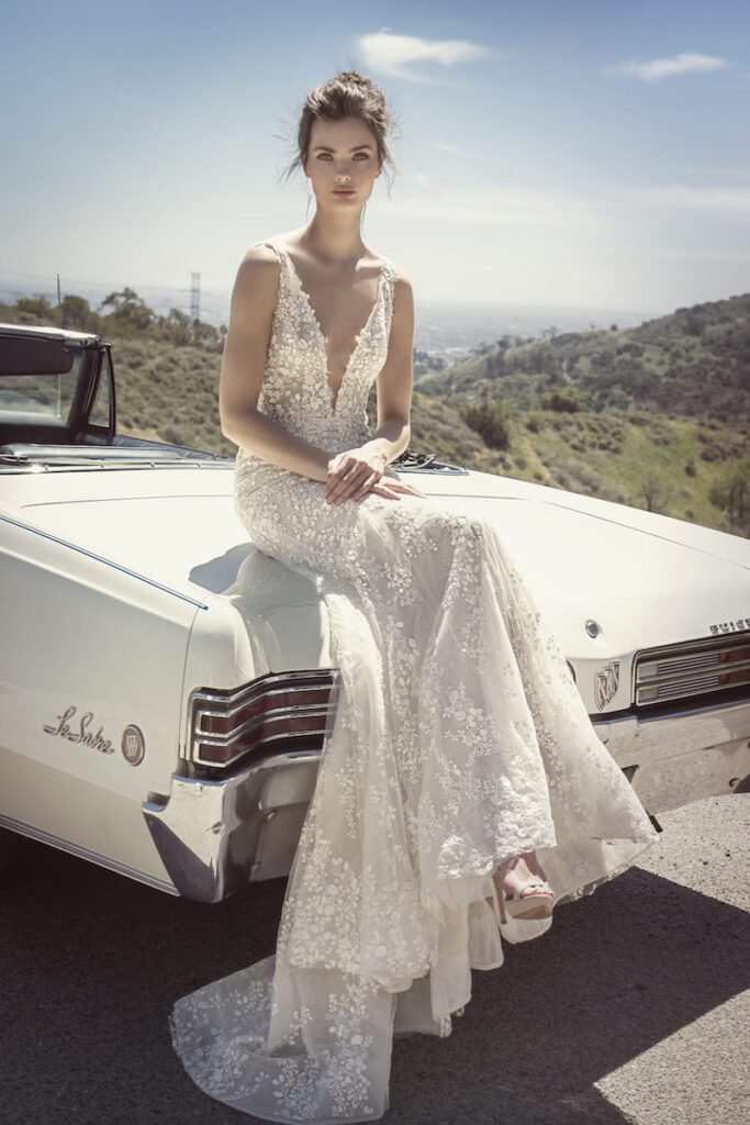 Woman in wedding dress sitting on white car