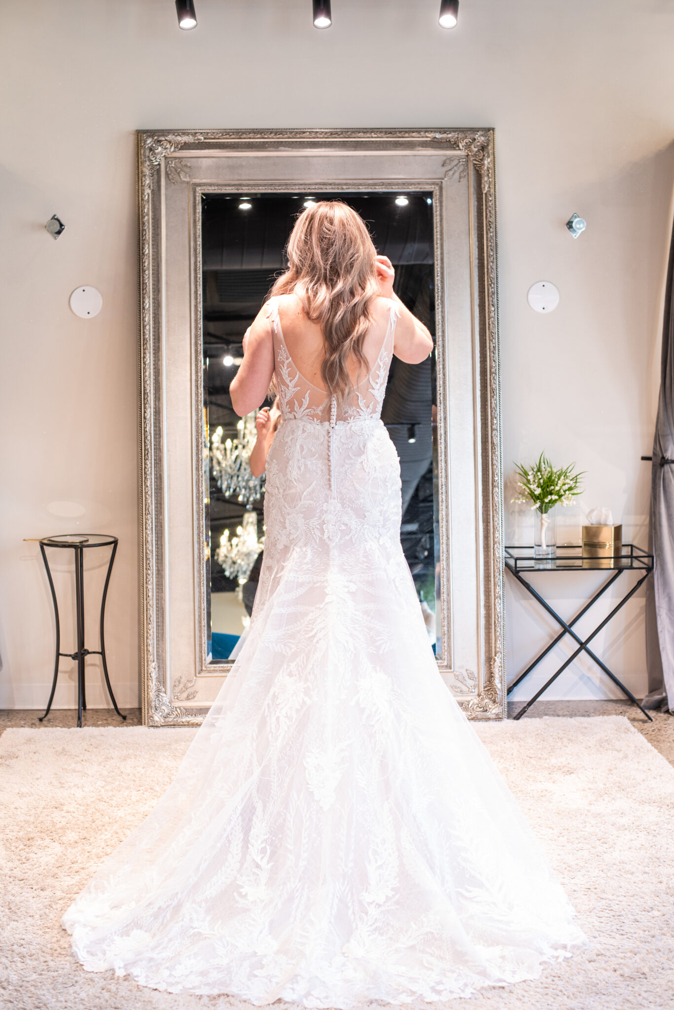 shot of woman's back as she checks herself out in mirror wearing white bridal dress