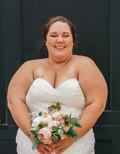 A woman in a wedding dress holding flowers, smiling towards the camera