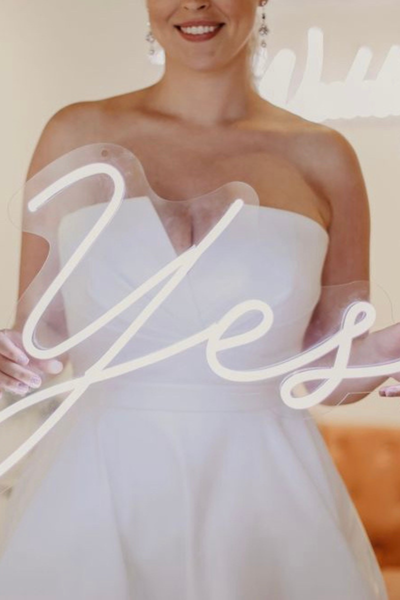 bride in bridal dress holding white neon sign spelling "Yes"