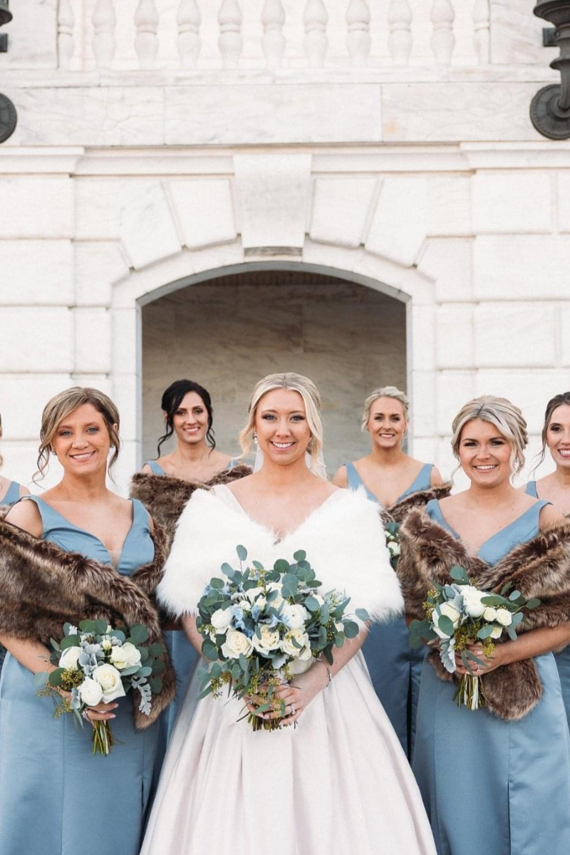 bride and her six bridesmaid posing with flower bouquets in front of building