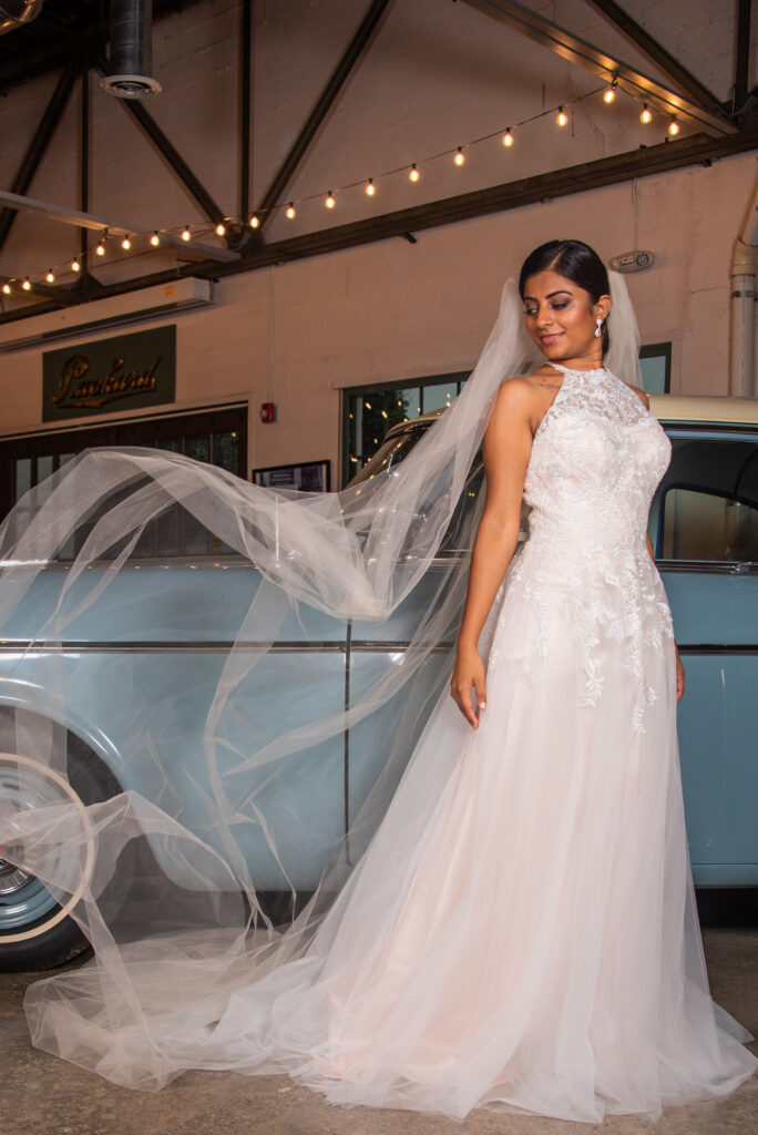 bride in front of vintage car ahas a flowing veil hair accessory