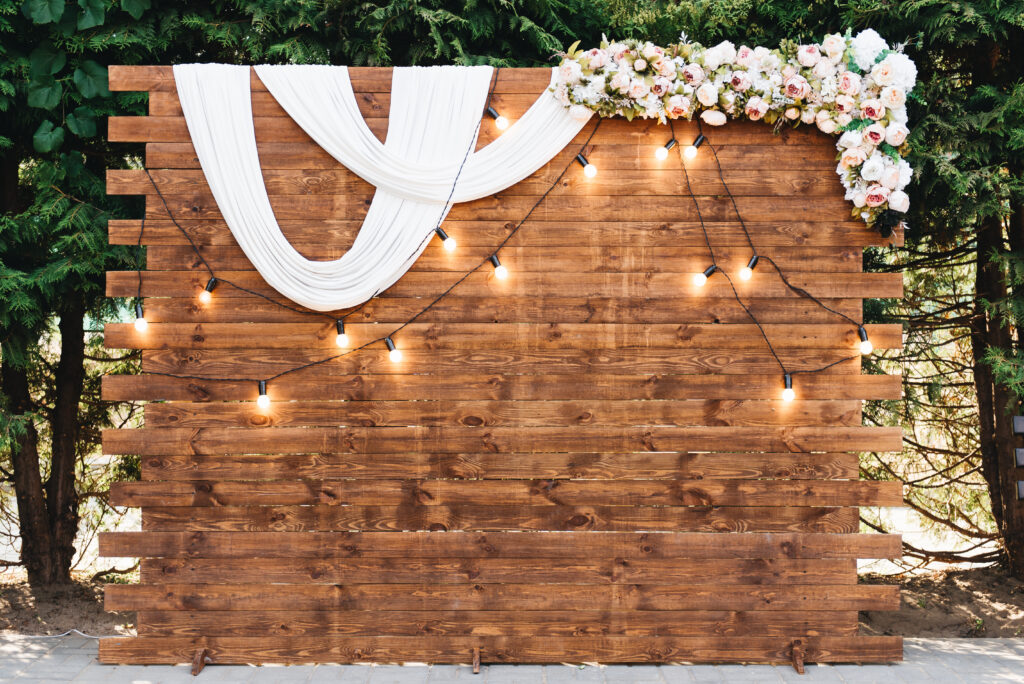 rustic wooden wall with draped fabric, lights, and flowers for wedding photo backdrop