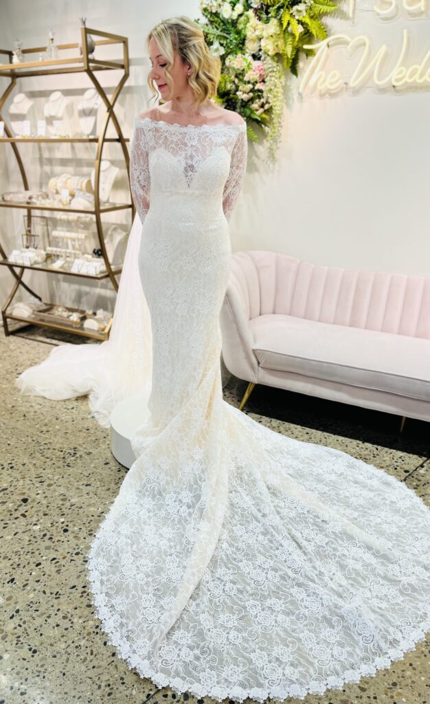 August is a delicate lace gown with a off the shoulder sleeves and a long train.