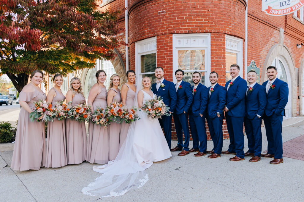 bridal party standing outside red brick building with the bride and bridesmaids holding bouquets of flowers