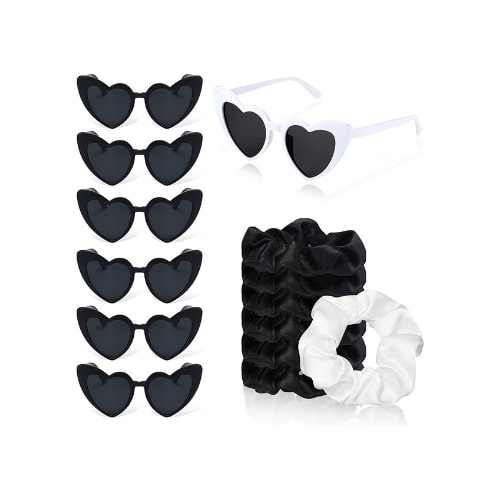On the left are heart shaped black sunglasses. On the right is a white pair of heart sunglasses and a stack of black hair scrunchies and one white scrunchie.