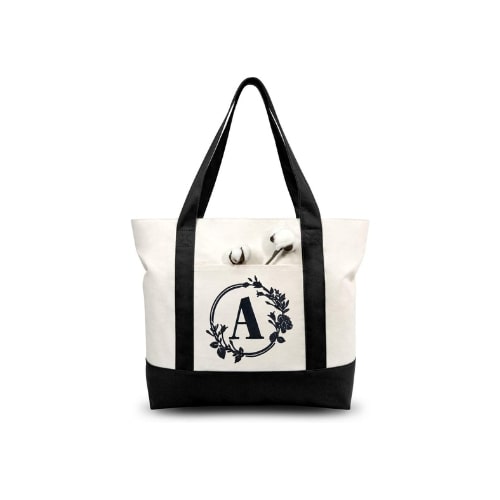 White and beige tote bag. The bottom and straps of the bag are black. In the middle of the bag is a black initial inside a circle.
