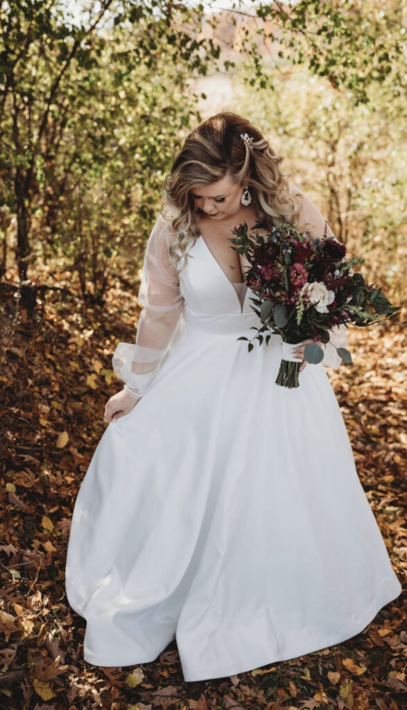 bride holding a bouquet of flowers walking through fallen leaves in autumn