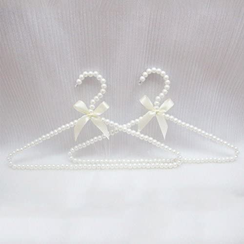 Two clothes hangers made of pearls. Around the joint of the hangers is an ivory bow.