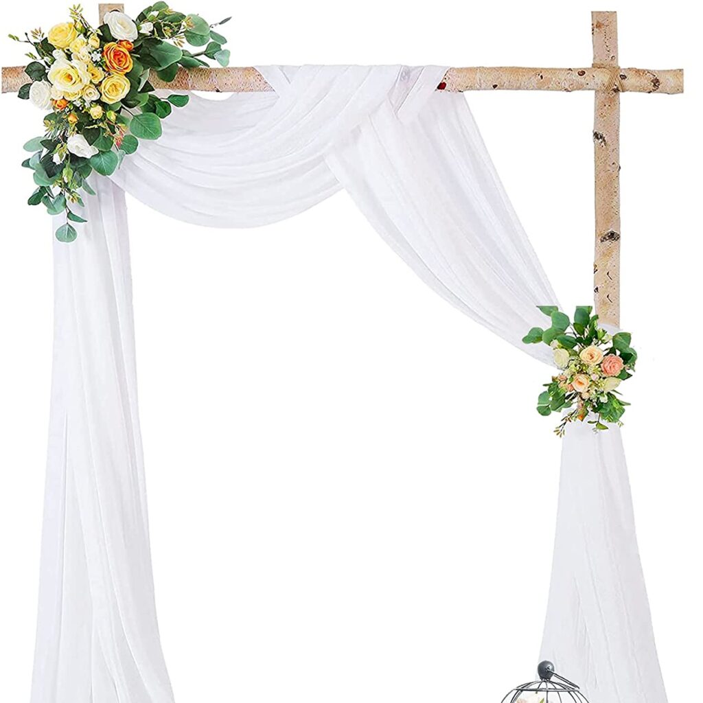 Rustic wedding arch made of knotty pine pieces. Draped on the wooden arch is a white drapery with yellow floral arrangements.