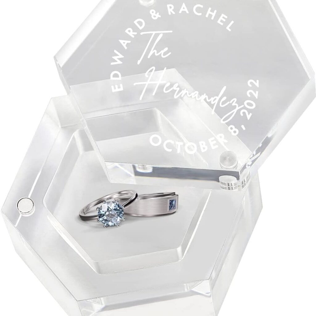 Glass, hexagonal wedding ring holder. On the lid are the bride and groom's name and wedding date. Inside is a silver set of wedding bands with crystal blue stones.