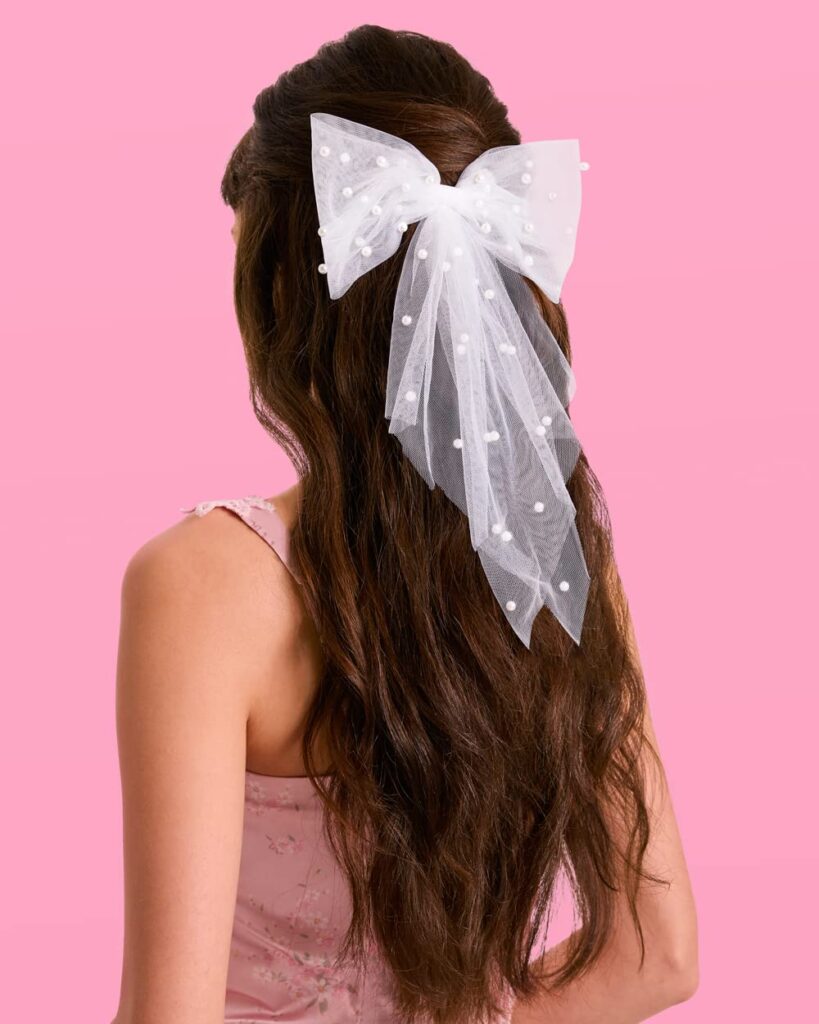 A girl with long curly, brunette hair. In her hair is a large white bow with small white polka dots.