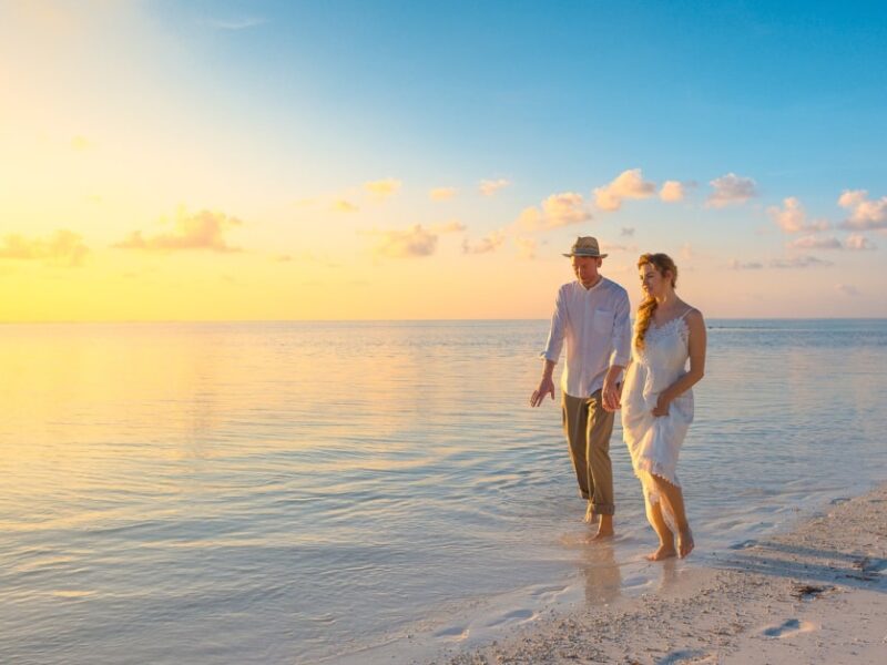 newly married couple walking along a beach at sunrise on their honeymoon