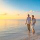 newly married couple walking along a beach at sunrise on their honeymoon