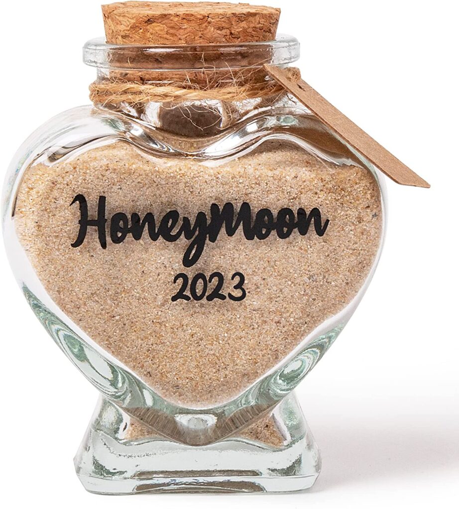 Small, heart shaped glass with cork stopper and twine around the neck. The glass is fild with sand and says "honeymoon 2023"