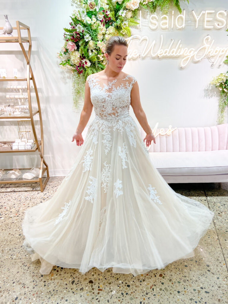 Bride wearing off white wedding dress with lace applique on bodice and waist line and tapering off on the tulle skirt.