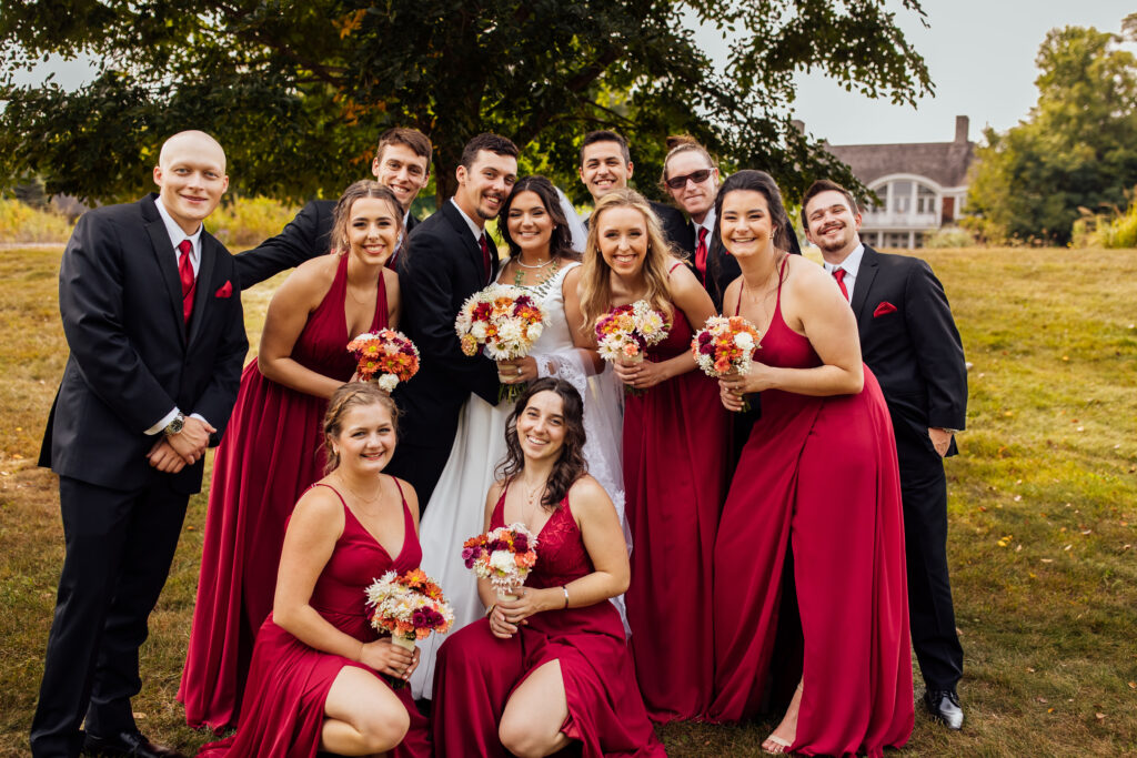 bridal party outside on the grass with bride and bridesmaids holding bouquets of white, orange, and red flowers