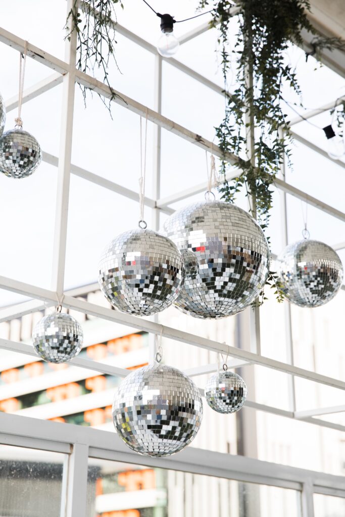 several sparkling disco balls hanging from rafters with greenery draped downward