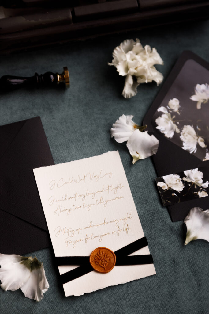 wedding invitation with a seal and black ribbons with white flower petals