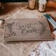 rustic wedding guest book with three pens next to it on a burlap table covering
