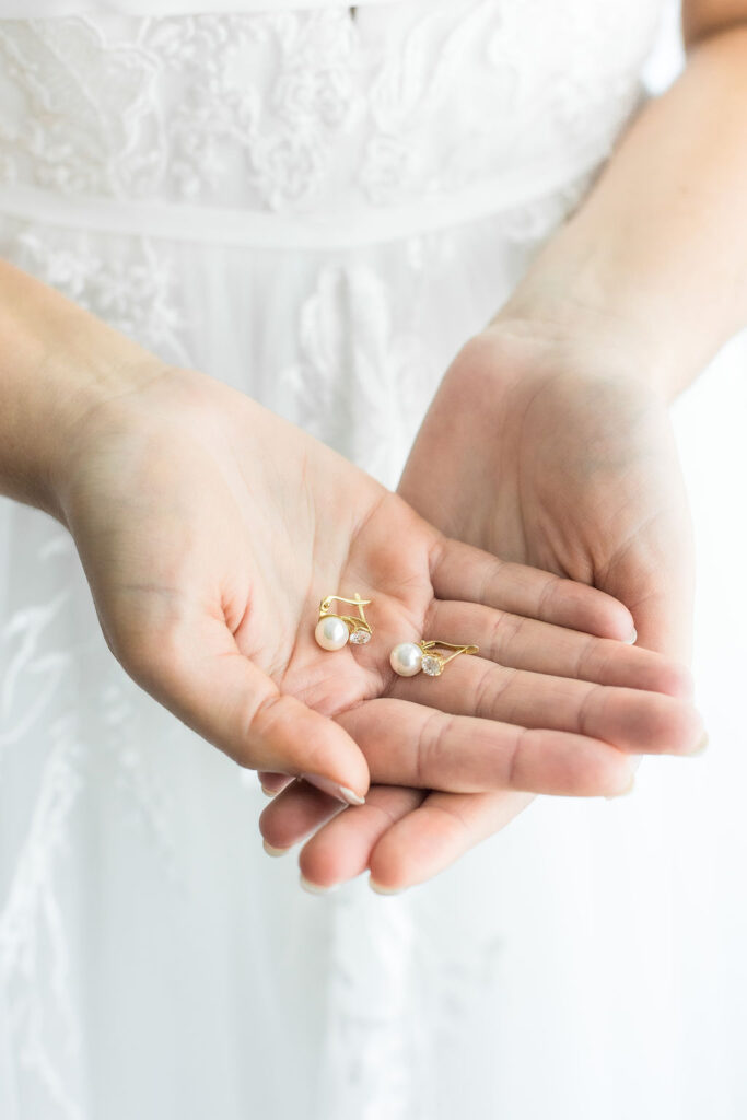 Alexa, a The Wedding Shoppe bride, holding two pearl earrings wearing a wedding dress
