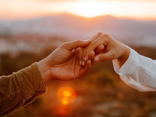 couple holding hands in front of a mountain range with the setting sun in the background
