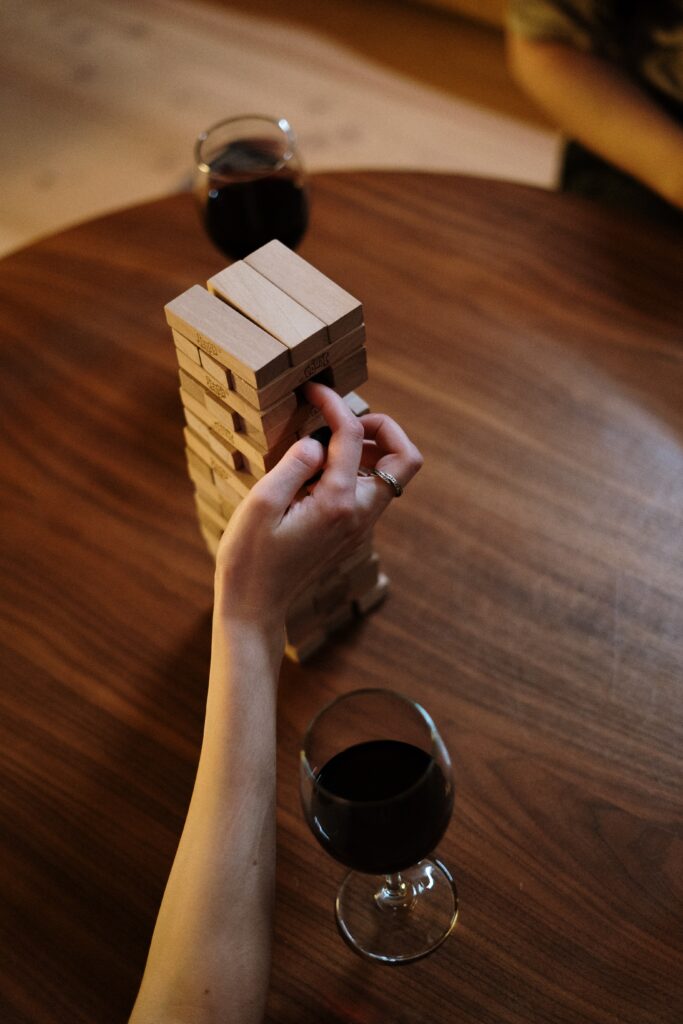 woman playing Jenga wearing a ring on her middle finger with two glasses of wine on the table
