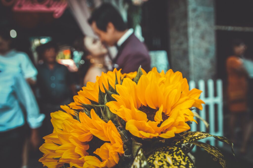 yellow sunflowers at a wedding with a couple kissing in the background
