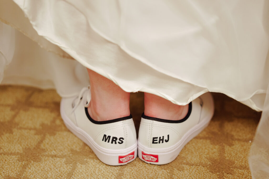Emily, a The Wedding Shoppe bride, wearing a pair of white Vans that say "MRS EHJ"