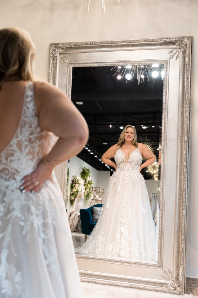 a woman looking at herself in the mirror wearing a floral wedding dress in The Wedding Shoppe