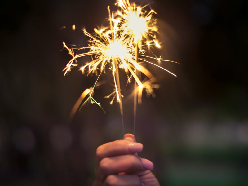 woman with pink fingernails holding a pair of sparklers at night