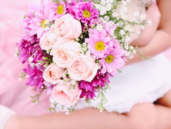 a little girl on a pink blanket with a bouquet of flowers.