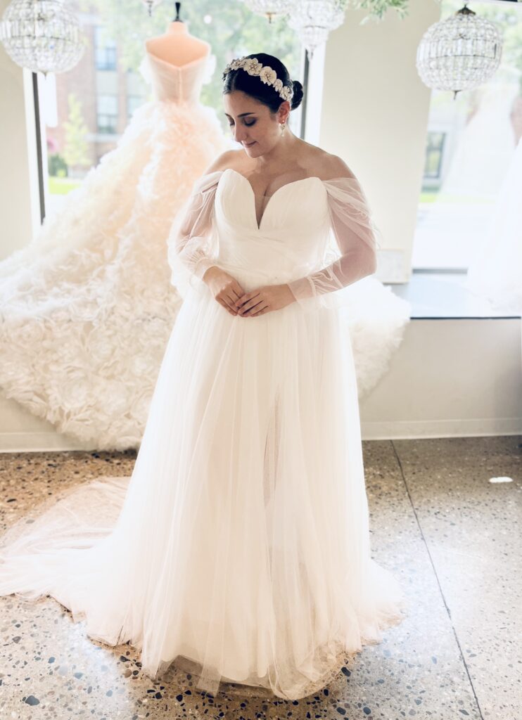 Shirley is a soft tulle gown with off the shoulder sleeves and a slit.