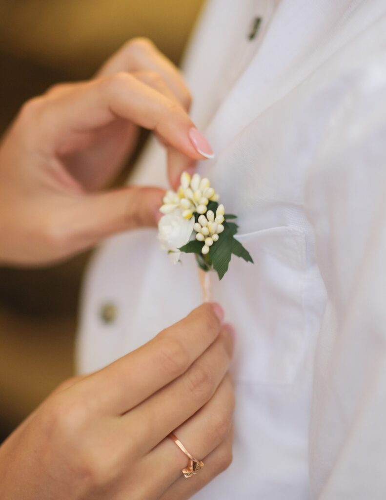 bride pinning a boutonniere to the shirt of her groom