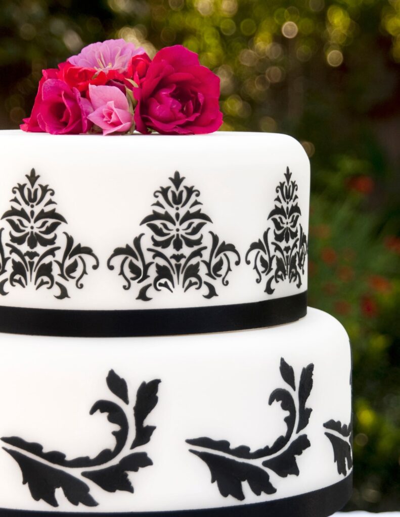 black and white cake with stenciled accents and bright red and pink flowers on top