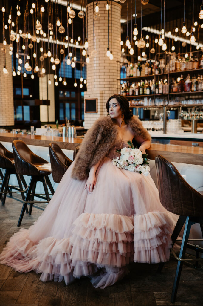 bride wearing a blush winter wedding dress and a fur jacket with a bouquet of flowers