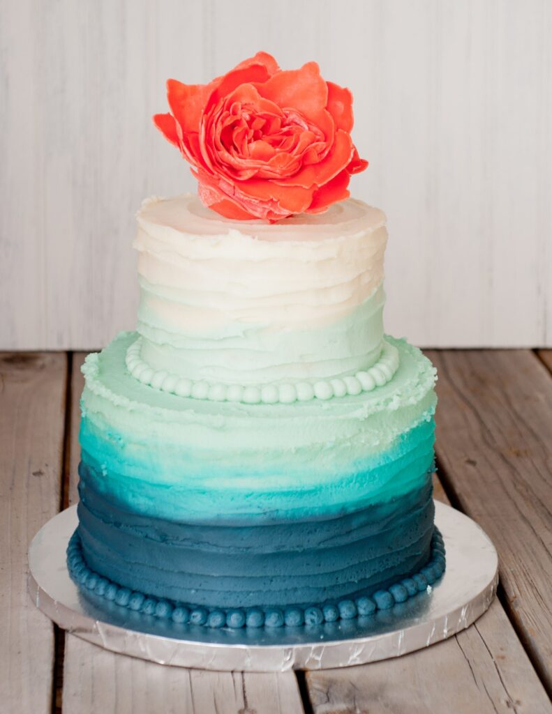 wedding cake inspired by shades of the ocean with an orange flower on top