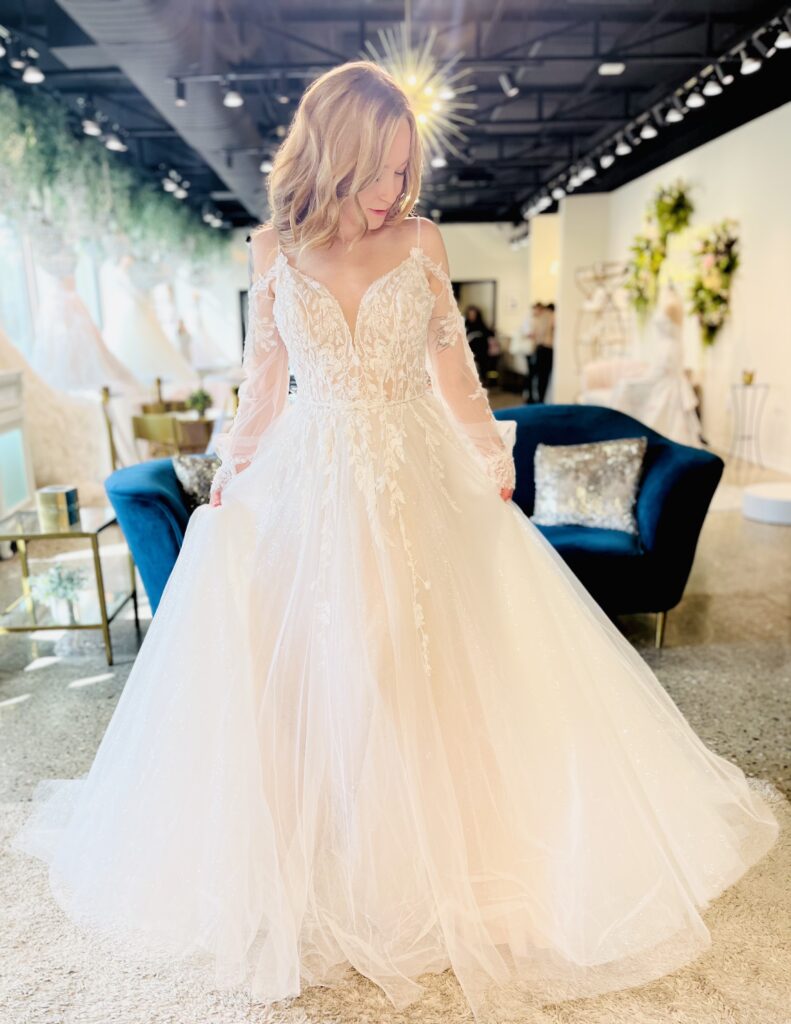 Claire is a fuller Aline with a sparkle tulle that sparkles like the snow when the sun hits it! Flowy off the shoulder sleeves are a perfect addition to this beautiful gown
